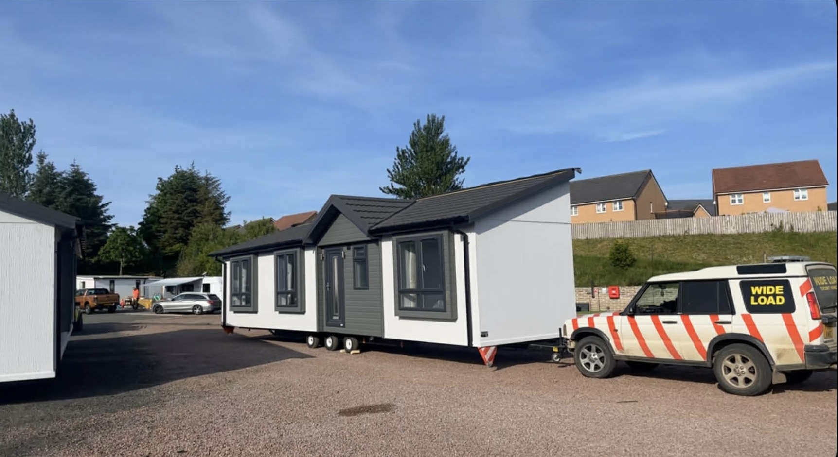 Modern park home with wide load escort SUV — modular home delivery UK